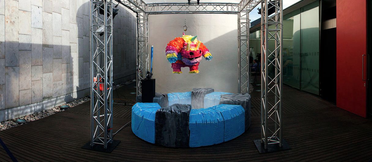 A piñata hanging in a truss rig, with the bat machine beside it